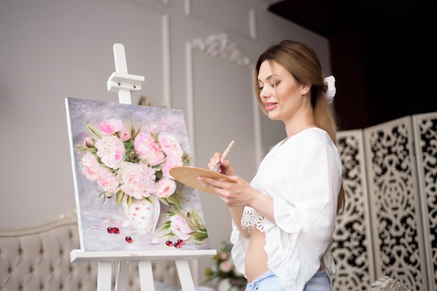 Portrait of a young pragnant woman painting with oil paints on white canvas, side view portrait