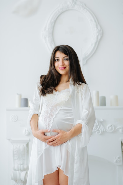 Portrait of young pregnant attractive woman, standing by the window, dressed in casual clothing, day before due date