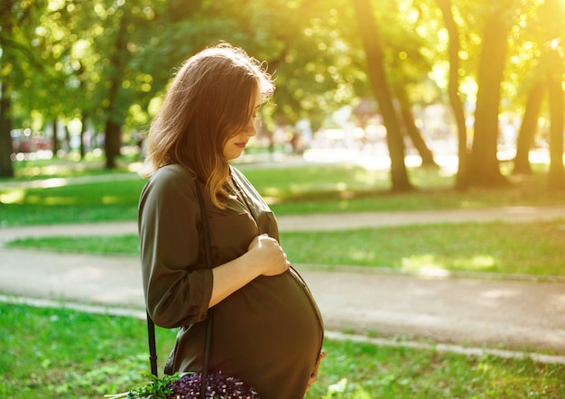 Portrait of young pregnant woman looking at her belly in a park 