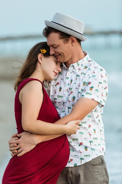 Portrait of young pregnant woman with husband with her head on his shoulder on the beach