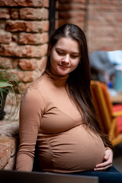 Portrait of young pregnanty woman freelancer using laptop computer for distance job while sitting in modern coffee with cup of tea