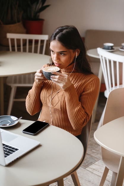 コーヒーを飲むラップトップコンピューターを使用して屋内のカフェに座っている若いかなり美しい女性の肖像画。