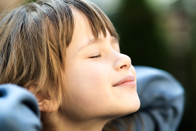 Portrait of young pretty child girl with long hair enjoying warm sunny day in summer outdoors. Cute female kid relaxing on fresh air outside.