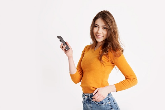 Портрет молодой красивой девушки в желтый свитер с телефоном в руках. Девушка общается с помощью мобильного телефона