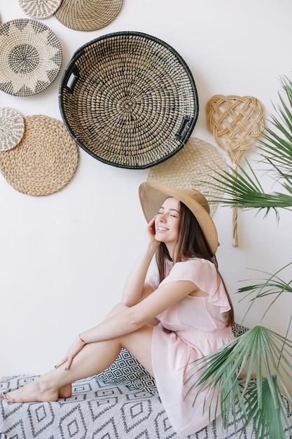 Portrait of a young pretty happy woman in a pink dress and a straw hat with rustic background