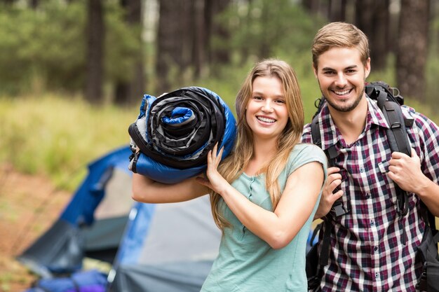 Portrait of a young pretty hiker couple holding a sleeping bag and backpack