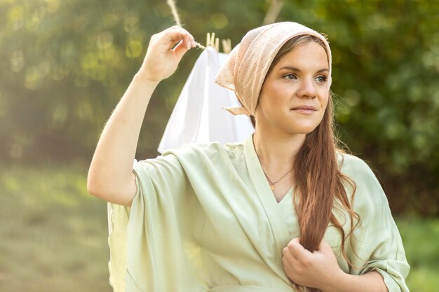 Portrait of young pretty white woman hanging up laundry on clothes line outside drying bed linens