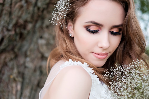 Portrait of young pretty woman (bride) in white wedding dress outdoors, make up and hairstyle