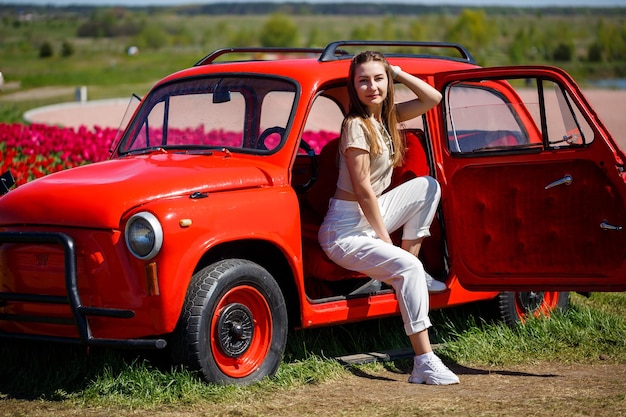 Portrait of young pretty woman leaning over rustic cabriolet car in colorful tulip fields Chilliwack Tulip Ftstival British Columbia Canada