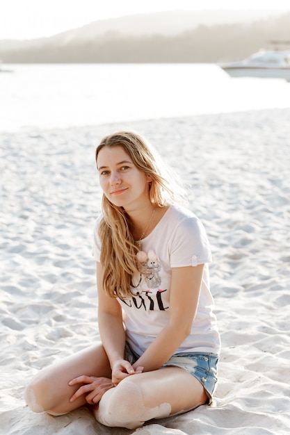 Portrait of young pretty woman sitting on the beach and looking