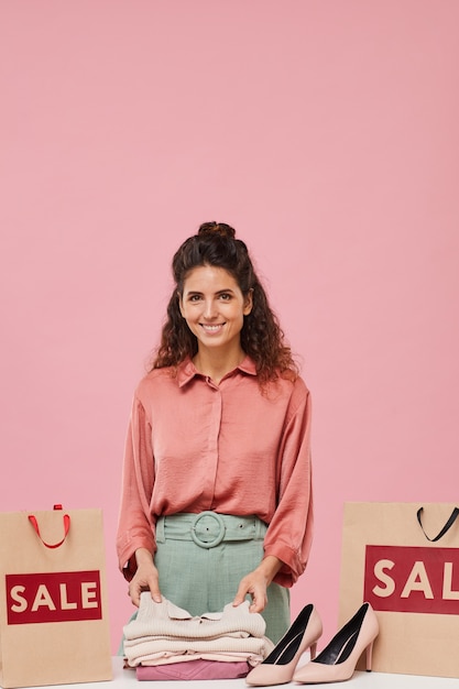 Foto ritratto di giovane donna graziosa con capelli ricci sorridente mentre levandosi in piedi vicino alle borse della spesa con vestiti nuovi