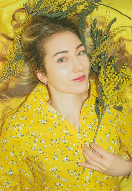 Portrait of young pretty woman with mimosa on the yellow background closeup