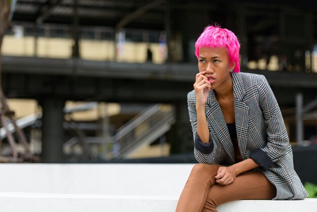 Portrait of young rebellious Asian businesswoman with pink hair in the city streets outdoors