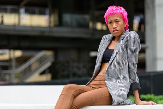 Portrait of young rebellious Asian businesswoman with pink hair in the city streets outdoors