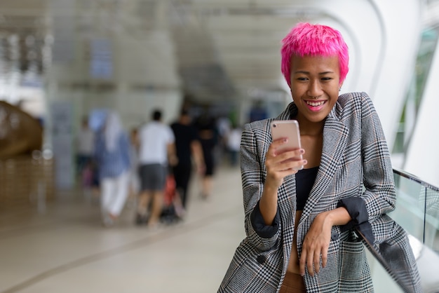 Portrait of young rebellious Asian businesswoman with pink hair at footbridge in the city outdoors