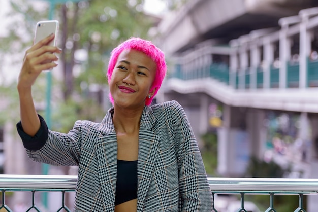 Portrait of young rebellious Asian businesswoman with pink hair at footbridge in the city outdoors