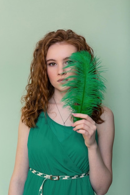 Portrait of a young red-haired beauty girl with a feather near her face