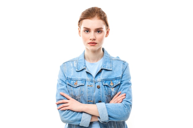 Ritratto di una giovane ragazza dai capelli rossi su sfondo bianco isolato in jeans. guarda nella telecamera