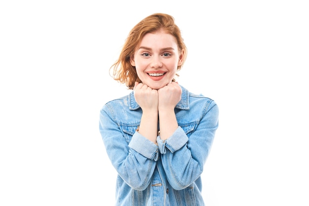 Portrait of a young red-haired girl on a white isolated background in jeans. Looks into the camera