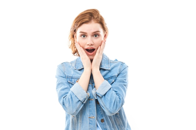 Portrait of a young red-haired girl on a white isolated background in jeans. Looks into the camera