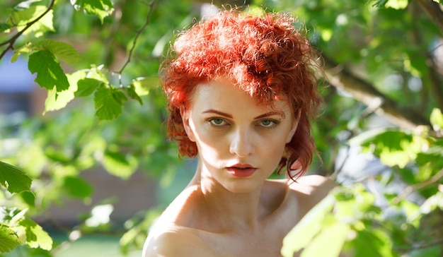 Portrait of a young red-haired woman among the foliage of trees illuminated by the suns rays