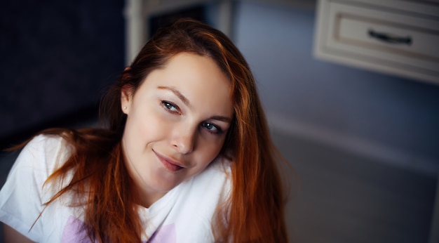 Photo portrait of young red-haired woman with perfect smooth skin. face of beautiful girl, close-up. female model in white t-shirt looks at camera and smiles.