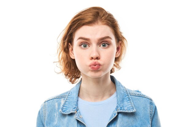 Portrait of young redhead woman puffing cheeks with funny face isolated on white studio background Humor concept mouth inflated with air crazy expression