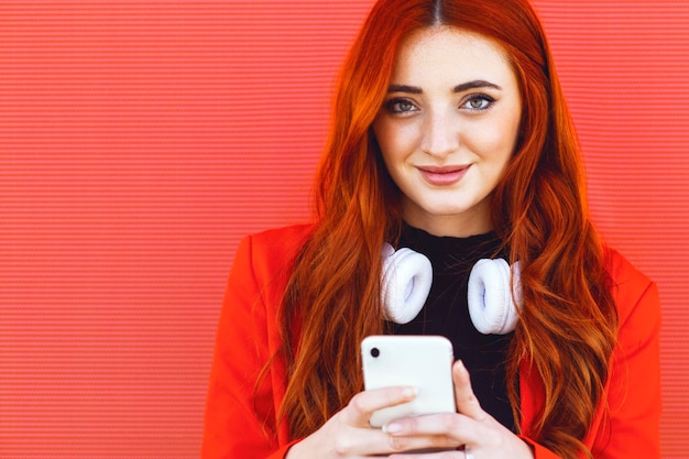 Portrait of young redhead woman smiling with elements of\
technology wireless headphones and smart