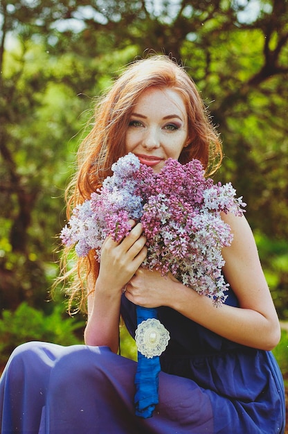 Photo portrait of young redhead woman in spring garden. freckles. blooming purple flowers. lilacs bouquet