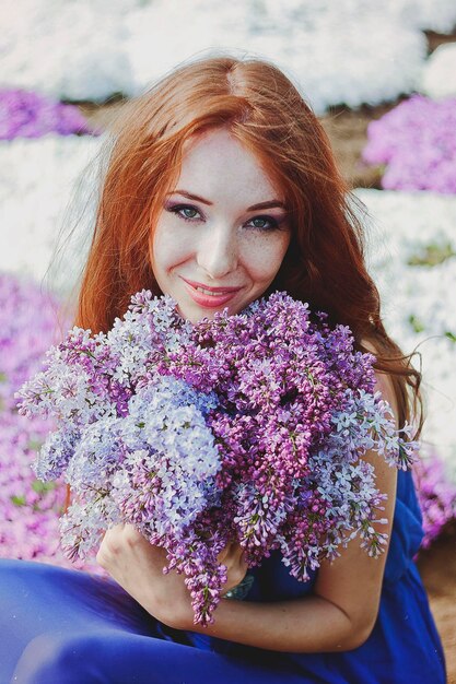 Portrait of young redhead woman in spring garden. freckles. blooming purple flowers. Lilacs bouquet