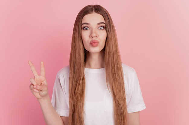 Portrait of young romantic woman showing two fingers victory gesture send air kiss