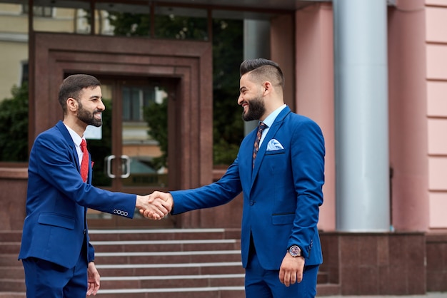 Portrait of a young saudi businessman greeting his business partner with a handshake in front of the business center outdoors