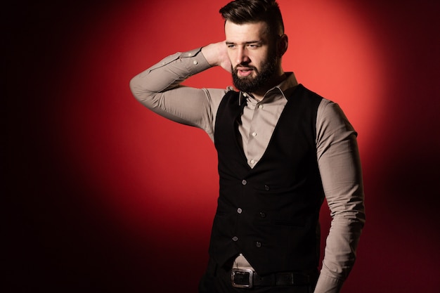 Portrait of a young serious bearded man in a black vest on red background. Space for text