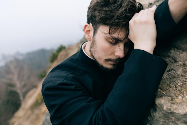 Portrait of a young serious Christian Catholic priest or pastor in a black robe outdoors