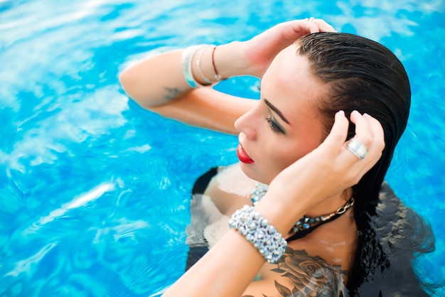 Portrait of a young sexy woman posing in water in a swimming pool with wet hair