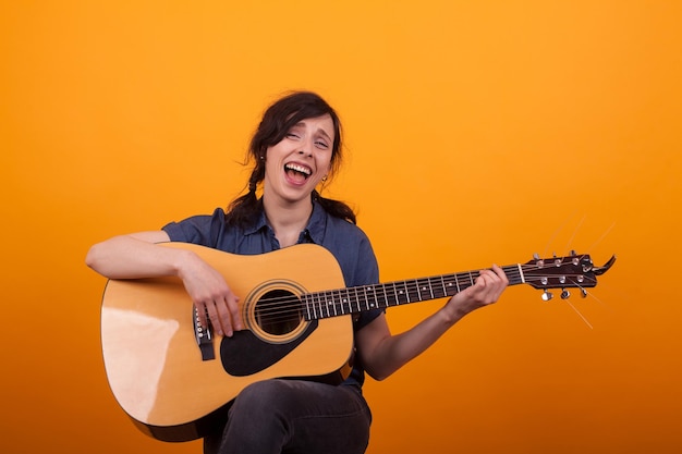 Portrait young singer with acustic guitar in studio over yellow background. Cheerul young artist with her guitar.