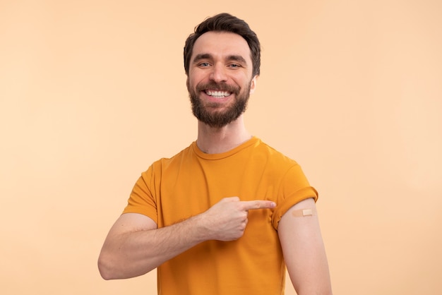 Foto ritratto di giovane uomo sorridente che punta al suo adesivo del vaccino