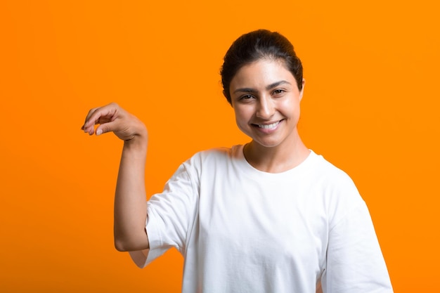 何か広告テンプレートを保持していることを示す空の手のひらを持つ若い笑顔の大人のインドの女性の肖像画