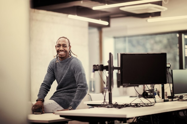 현대적인 시작 사무실에서 사무실 책상에 앉아 웃고 있는 젊은 아프리카계 미국인 남성 소프트웨어 개발자의 초상화
