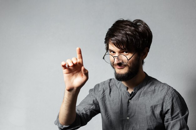 Portrait of young smiling bearded guy with disheveled hair, wearing grey shirt and glasses