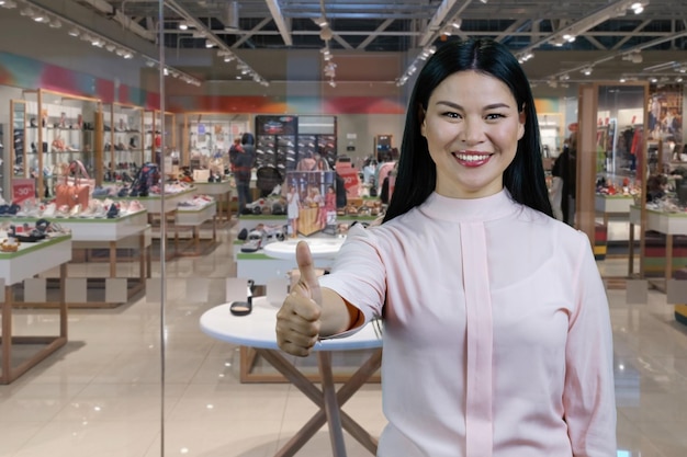 Portrait of a young smiling brunette asian woman shows thumb up