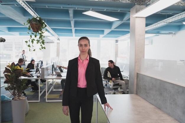 Портрет молодой улыбающейся деловой женщины в творческом открытом коворкинг-офисе. Успешная деловая женщина, стоящая в офисе с копирайтом. Коллеги работают в фоновом режиме.