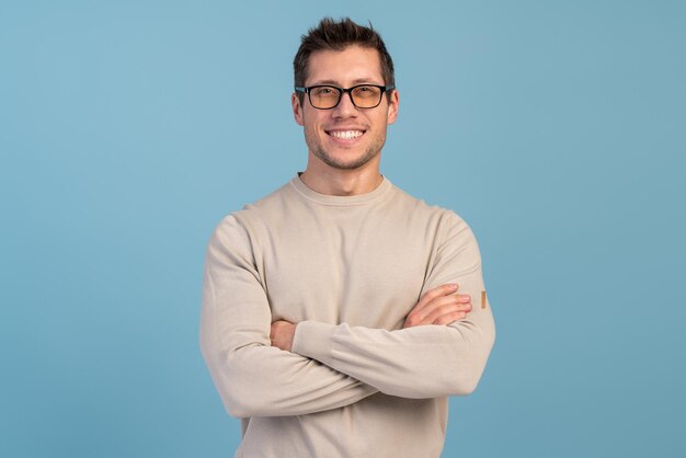 Portrait of young smiling caucasian man with crossed arms wearing casual closes posing isolated on blue background