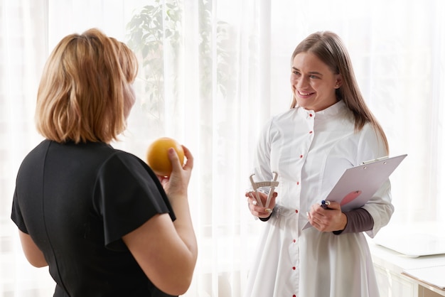 Portrait of young smiling female nutritionist in the consultation room. Making diet plan. Young woman visiting nutritionist in weight loss clinic