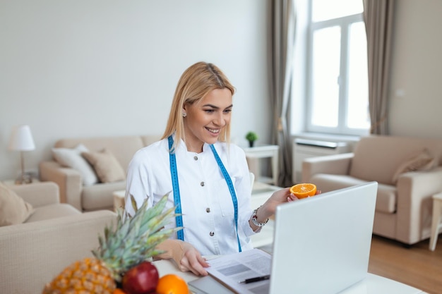 Ritratto di giovane nutrizionista femminile sorridente nella sala di consultazione scrivania nutrizionista con succo di frutta sano e nastro di misurazione dietista che lavora sul programma di dieta