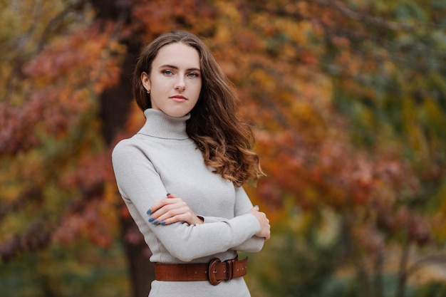 Ritratto di giovane ragazza sorridente in un vestito grigio al parco d'autunno