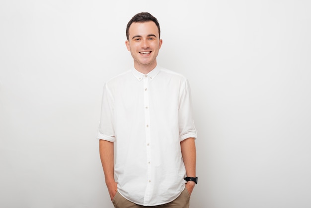 Photo portrait of a young smiling guy who is holding his hands in his pants pockets on white background.