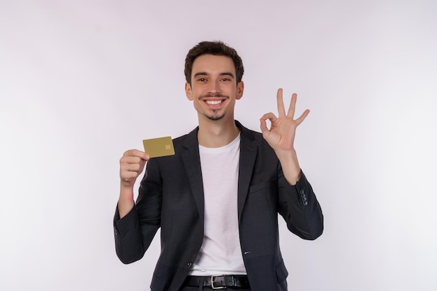 Portrait of Young smiling handsome businessman showing credit card and ok sign hand isolated over white background