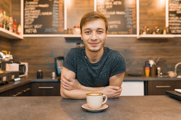 Портрет молодого улыбающегося мужского работника кафе, стоя у прилавка