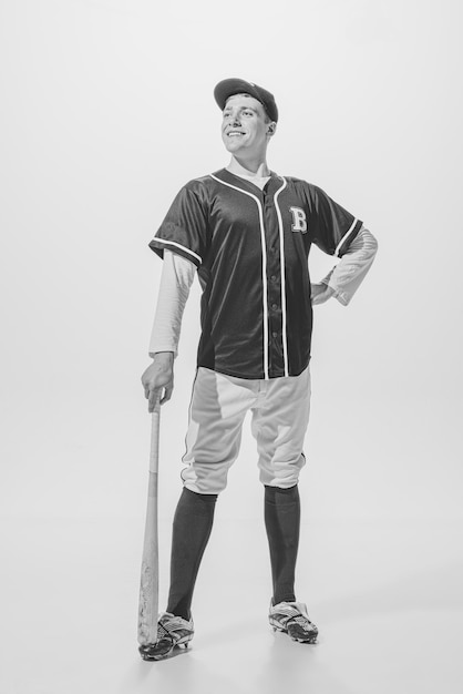 Портрет молодого улыбающегося бейсболиста в форме, позирующего с битой в черно-белой фотографии